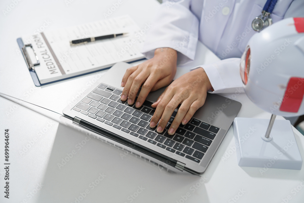 A doctor's hands are seen typing on a laptop keyboard with a stethoscope around the neck on white desk. - obrazy, fototapety, plakaty 
