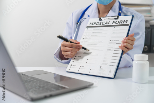 A doctor in a lab coat with a stethoscope is holding a medical form on a clipboard and pointing to it with a pen. photo