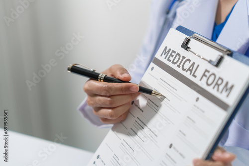 A doctor in a lab coat with a stethoscope is holding a medical form on a clipboard and pointing to it with a pen. photo