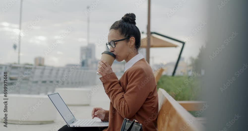 Slow motion of Middle Eastern businesswoman working with laptop and drinking take away coffee outdoors in city. Business and urban lifestyle concept. Slow motion of Middle Eastern businesswoman working with laptop and drinking take away coffee outdoors in city. Business and urban lifestyle concept.