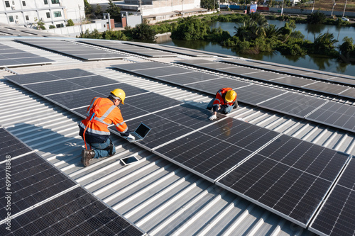 Two caucasian engineering technician is a professional trained in skills and techniques installing solar photovoltaic panels system on industrial factory roof, Engineering concepts to good environment