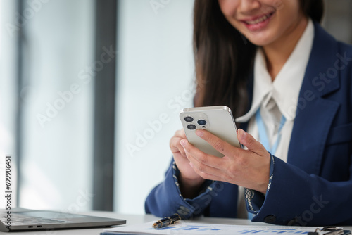 businesswoman's hands holding a pen and smartphone, with a calculator and documents on the desk.
