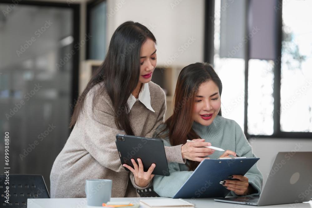 Two Asian individuals, possibly friends, studying together with a tablet and a laptop on the table. Two Asian individuals, possibly friends, studying together with a tablet and a laptop on the table.