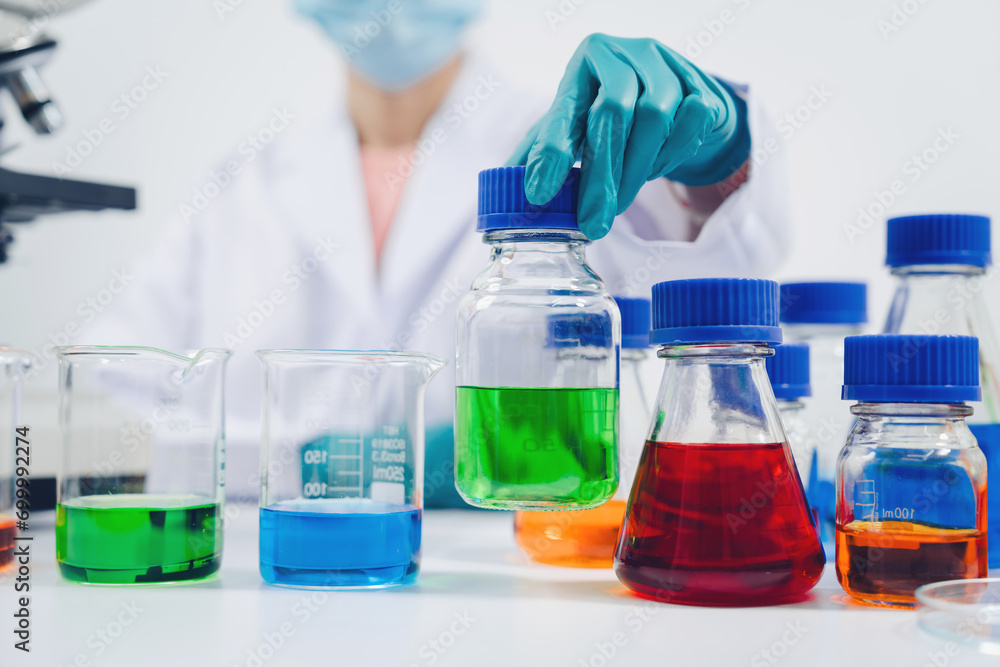 A scientist examines samples with a microscope in a laboratory with test tubes filled with colorful liquids in the background. A scientist examines samples with a microscope in a laboratory with test tubes filled with colorful liquids in the background.