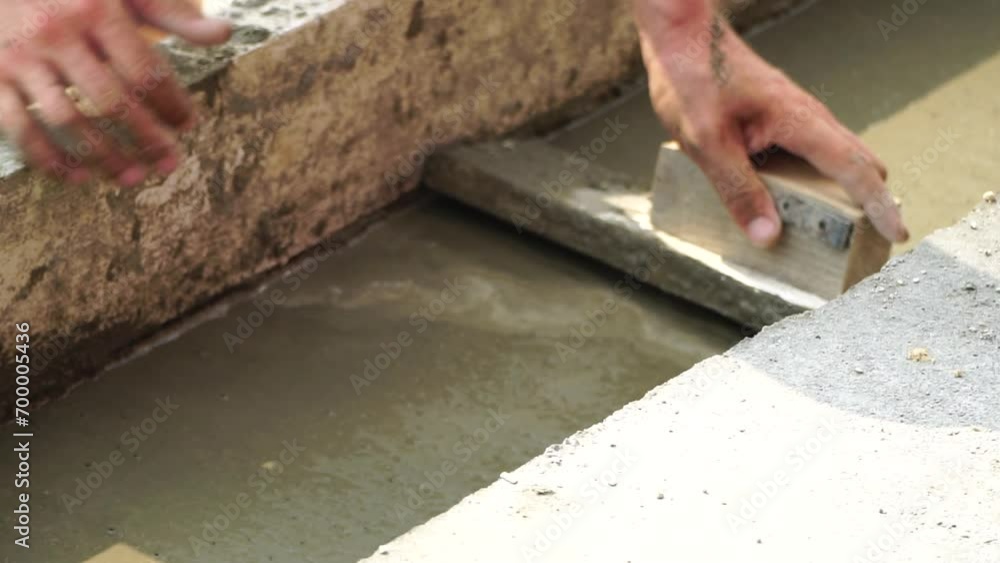 Construction, Worker Hands smooth wet cement in wooden frame at a construction site during daytime to ensure an even surface Construction, Worker Hands smooth wet cement in wooden frame at a construction site during daytime to ensure an even surface