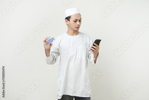 handsome asian man holding credit card and mobile phone on isolated background