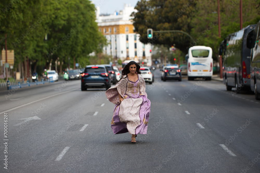 Beautiful Latin woman with long curly hair dressed in a 15th century dress running between cars on a big city avenue. The woman travels in time from the past to the present.