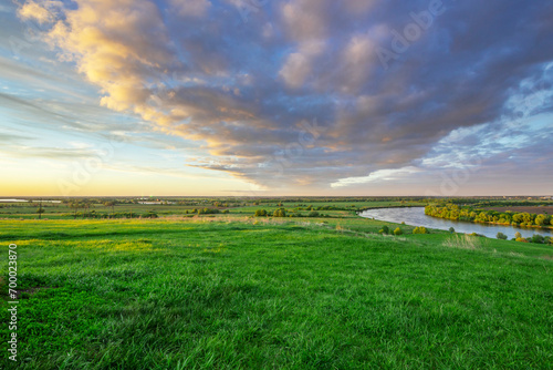 A river against a backdrop of green fields  a breathtaking view from the hill. Colorful sky with clouds during sunset. Landscape in spring. Nature during a bright sunset.
