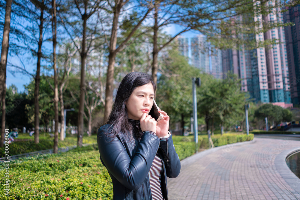 Beautiful woman with long hair in black leather jacket using mobile phone on the park Beautiful woman with long hair in black leather jacket using mobile phone on the park