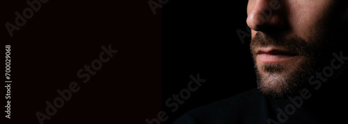 Close up serious brutal bearded man on dark background Close up of young bearded cool business guy standing against black background copy space photo