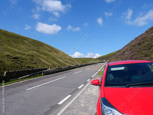 Unrecognizable woman sitting inside of red car parked on roadside of winding between hills Snake Road or Snake Pass in Peak District National Park of United Kingdom.
