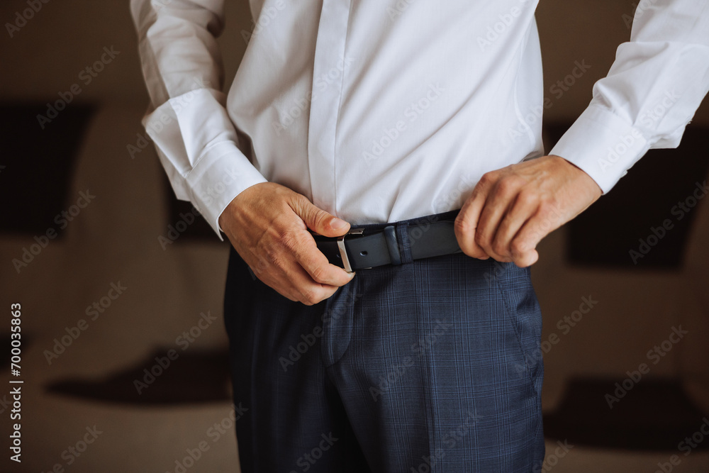 The morning of the groom, the groom prepares for the wedding ceremony, dresses in a suit and shoes. A man wears a fashionable black belt The morning of the groom, the groom prepares for the wedding ceremony, dresses in a suit and shoes. A man wears a fashionable black belt