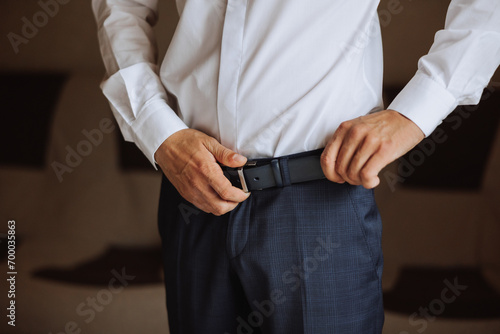 The morning of the groom  the groom prepares for the wedding ceremony  dresses in a suit and shoes. A man wears a fashionable black belt