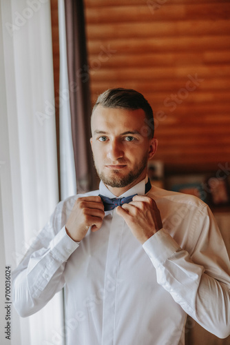 A stylish groom is tying his tie, preparing for the wedding ceremony. Groom's morning. A businessman wears a tie. The groom is getting ready in the morning before the wedding ceremony.