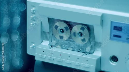 A cassette with gold reels plays music in a Hi-Fi recorder from 80s of silver  color. Closeup. Shot in motion photo