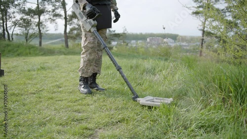 Military sapper with a metal detector in the field. Ukrainian Explosive Ordnance Disposal Officer detecting metal by metal detector device photo