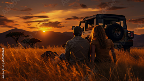 couple sitting on the floor Grass and a jeep in the grass field with wild animals in the background, the sunset. © ND STOCK