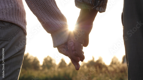 Close up silhouette of palms hands of elderly old people with wrinkles. Married couple of old people holding hands. Helping hand and support, feeling of love. Summer evening in park against sunset ray