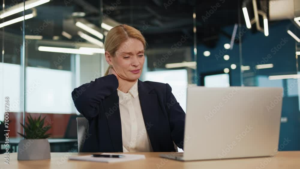 Tired businesswoman is experiencing neck pain while working in modern office. Female holding her neck with hand. Business lady having busy workday. Exhausted professional suffering from neck pain. Tired businesswoman is experiencing neck pain while working in modern office. Female holding her neck with hand. Business lady having busy workday. Exhausted professional suffering from neck pain.