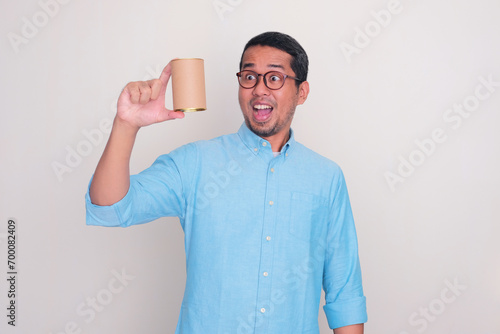 Adult Asian man looking to a can that he hold with amazed expression photo