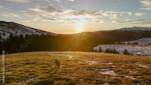 Couple hiking in the winter season with sunset in the background. Aerial back follow shot of people walking on yellow grass towards sunset photo