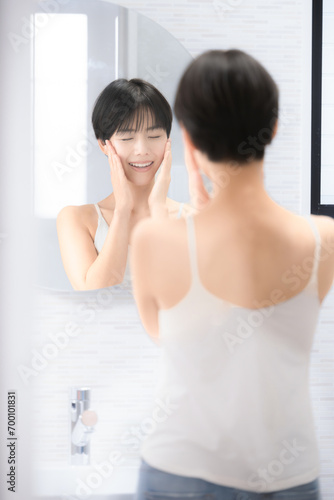 A beautiful woman looking into the mirror at a washbasin that is easy to use with images such as beauty, touching her cheeks with both hands while looking into the camera Vertical