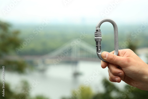 Man holding metal carabiner outdoors, closeup. Space for text photo