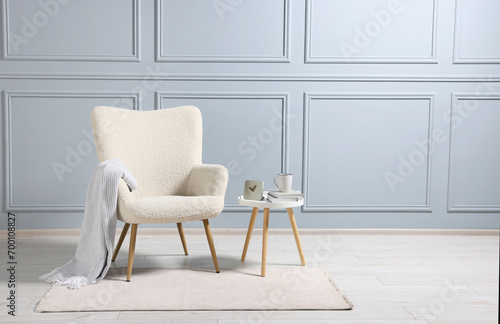 Comfortable armchair with blanket and side table indoors, space for text