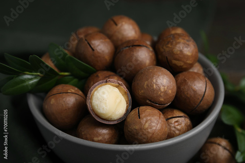Tasty Macadamia nuts and green twig in bowl on table, closeup