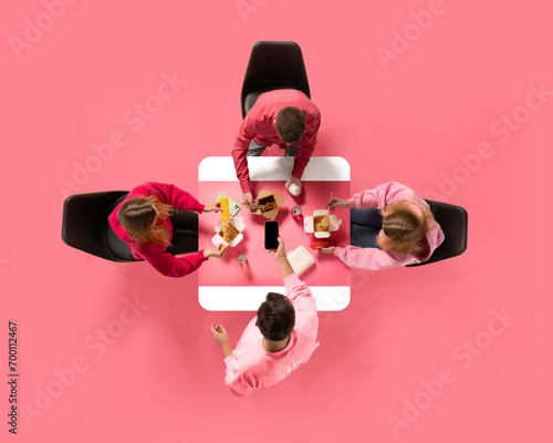 Creative collage. Aerial view of young people, colleagues eating delivery food against pink background. Copy space. Concept of business lunch, morning meeting, briefing. Ad photo