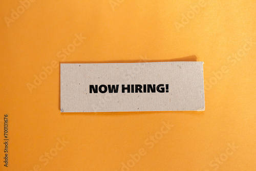 Now hiring lettering on ripped paper piece with orange background. Business recruitment concept. Top view, copy space.