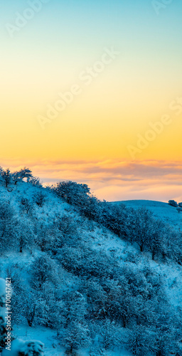 Background photo of low clouds in a mountain valley, vibrant blue and orange sky. Sunrise or sunset view of mountains and peaks peaking through clouds