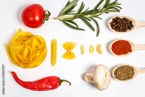 Raw pasta with spices and different vegetables on a white background