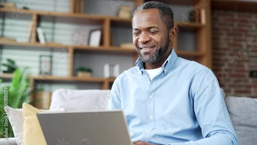Mature african american businessman talking on video call using laptop while sitting on sofa in living room at home office. A confident entrepreneur conducts a remote meeting with business partners photo