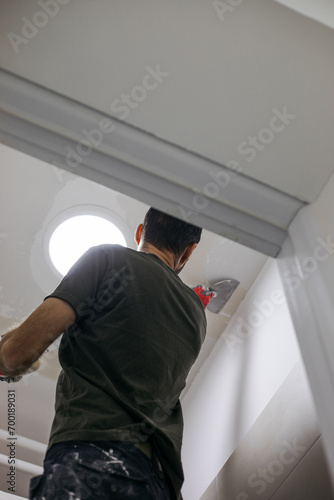 A man on a ladder plasters the wall and prepares it for painting. Plastering the wall and painting.
