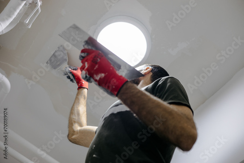 A man on a ladder plasters the ceiling and prepares it for painting. Wall plastering and painting.