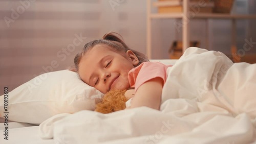 Adorable young girl asleep, embracing teddy bear in cozy bed, peaceful rest photo