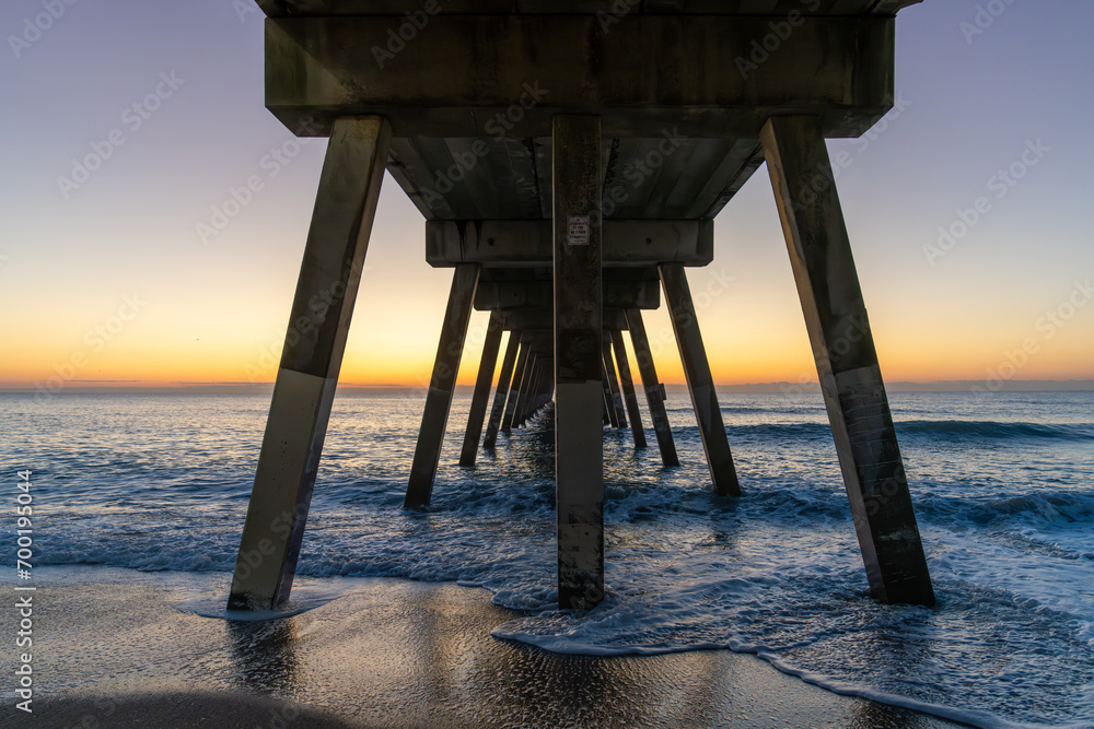 Sunrise illuminates a pier at Wrightsville Beach, casting long shadows over the ocean waves.