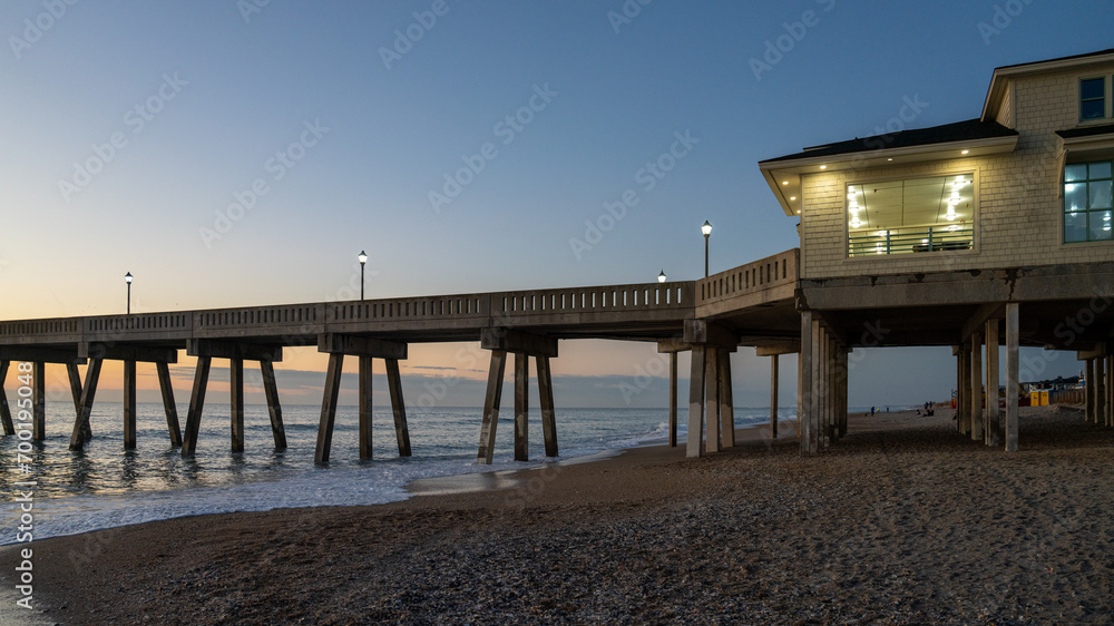 Sunrise illuminates a pier at Wrightsville Beach, casting long shadows over the ocean waves. Sunrise illuminates a pier at Wrightsville Beach, casting long shadows over the ocean waves.