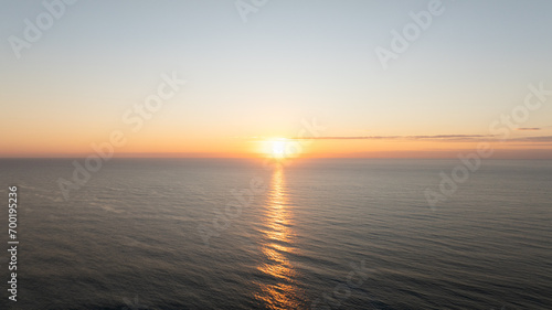 The sun sets over a calm sea, with its golden reflection stretching across the water to the horizon. © Red Lemon