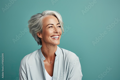 mujer madura de 50 años posando sonriente con una camisa gris claro verdoso, sobre fondo verde photo