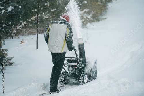 Foto A snowy suburban scene with a man using a snowblower to clear the sidewalk