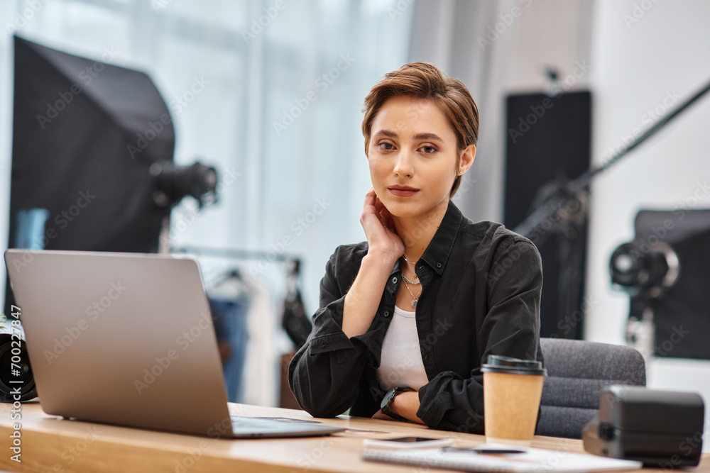 young beautiful woman in casual attire sitting at desk in her photo studio and looking at camera young beautiful woman in casual attire sitting at desk in her photo studio and looking at camera