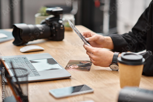 cropped view of camera and coffee on table next to young female photographer with photos in hands photo