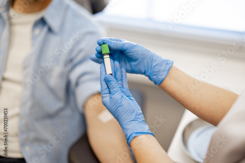 Laboratory assistant holds tube with blood for analysis, happy male patient on background, focus on a tube
