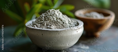 Close-up view of gray bentonite clay in a small white bowl, serving as a DIY mask and body wrap recipe for a natural beauty treatment and spa. photo