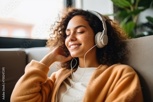 Pleased young woman in headphones listening to music while relaxing on sofa at home.