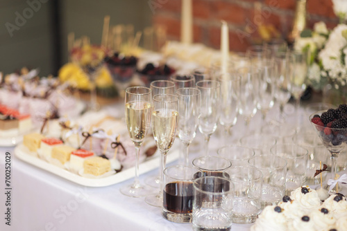 Party and holiday celebration concept. Many glasses of champagne on the table in the restaurant. Catering on wedding. Delicious fruits appetizers  desserts on stand  drinks  modern tab. 