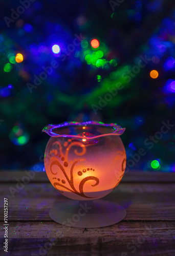 Glass candle light decoration on wood table with blured christmas tree on background