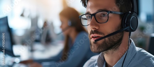Experienced male consultant improving company growth and feedback through research and reviews, using communication headset in an office setting, specializing in telesales, customer care, or tech photo